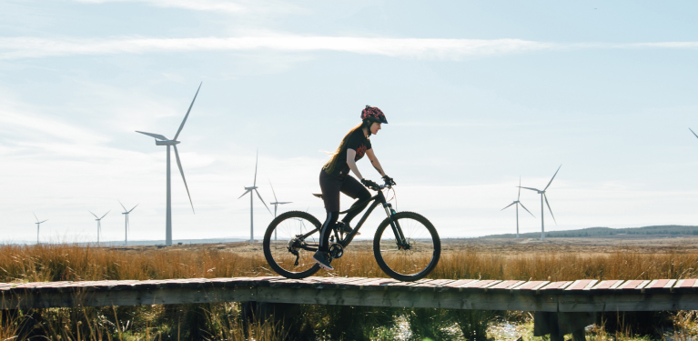 Photo d’une personne faisant du vélo dans un champs avec des éoliennes 